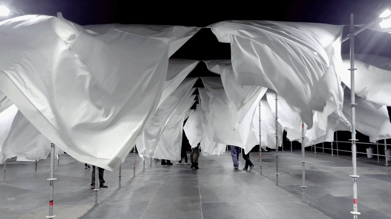 Animated GIF showing large white sheets waving vigorously on a scaffolding structure at night.