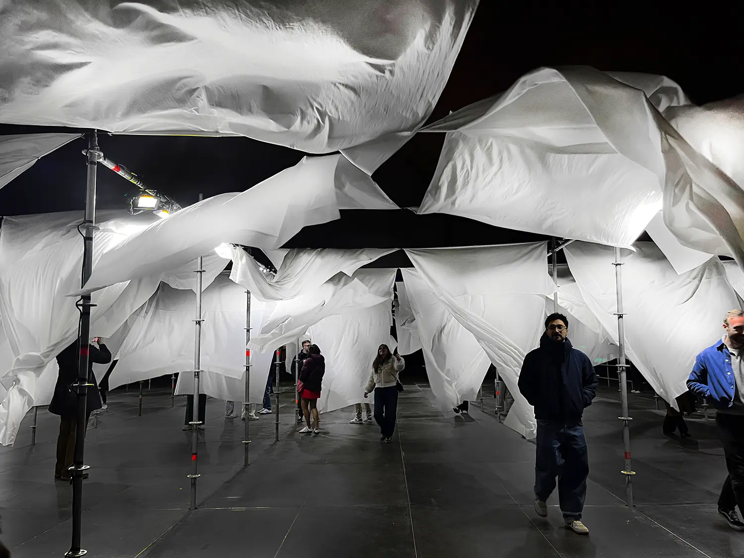 People walking through a glowing fabric installation at night under artificial lighting.
