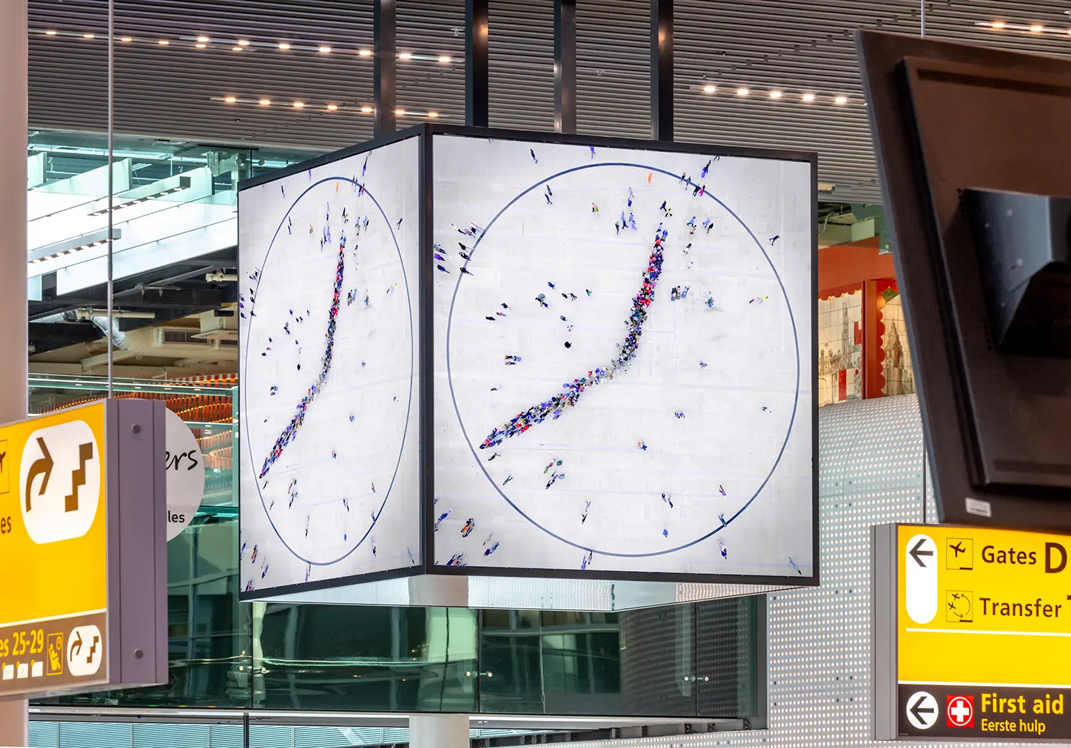 Close-up view of the cubic video installation at Schiphol Airport, showing the circular clock face composed of hundreds of small human figures.