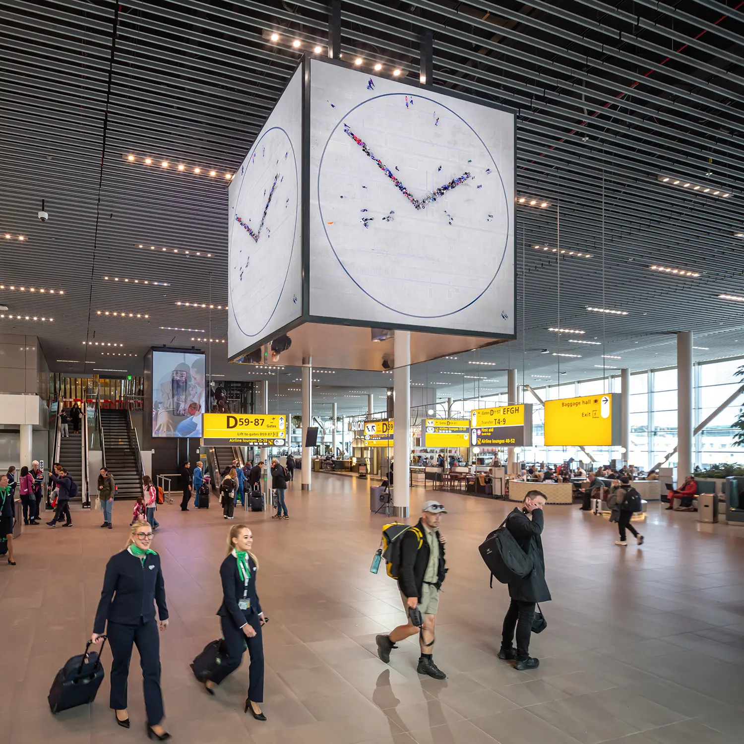 Perspective view of the Schiphol terminal with airport crew walking past the monumental Maarten Baas clock installation.