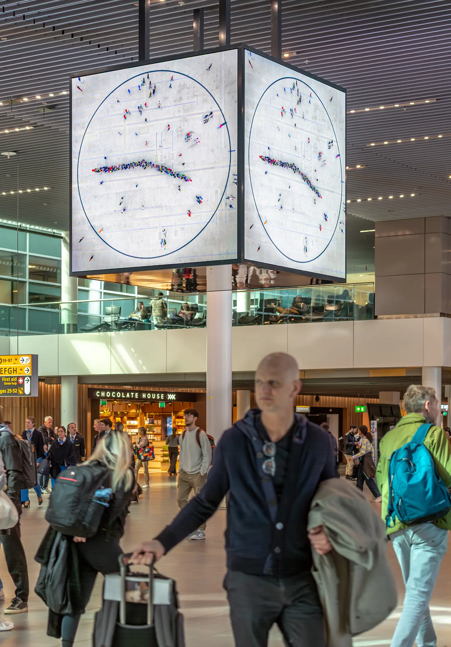 Travelers moving through Lounge 1 with the Maarten Baas People’s Clock in the background, showing the clock hands at a horizontal position.