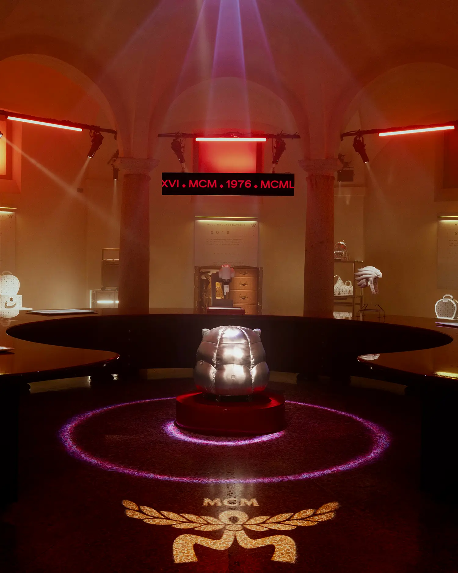 An exhibition room with a silver metallic pouf centered in a neon ring light.