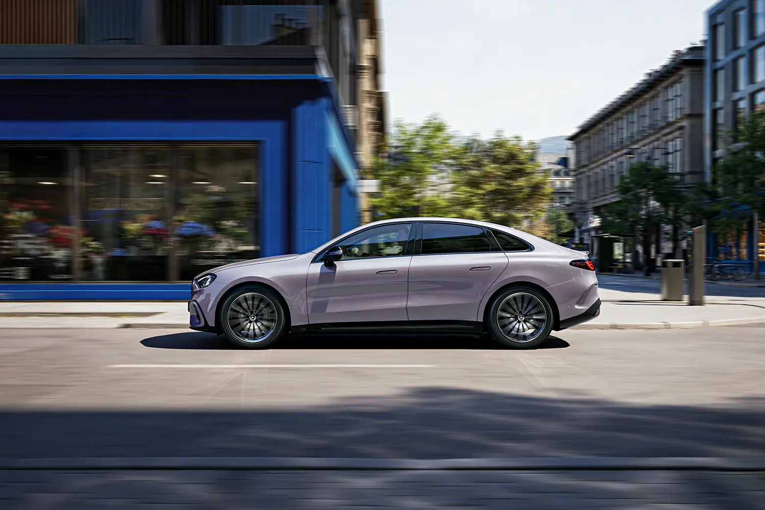 Full side profile of the Mercedes-Benz electric C-Class in motion on a sunlit urban road.