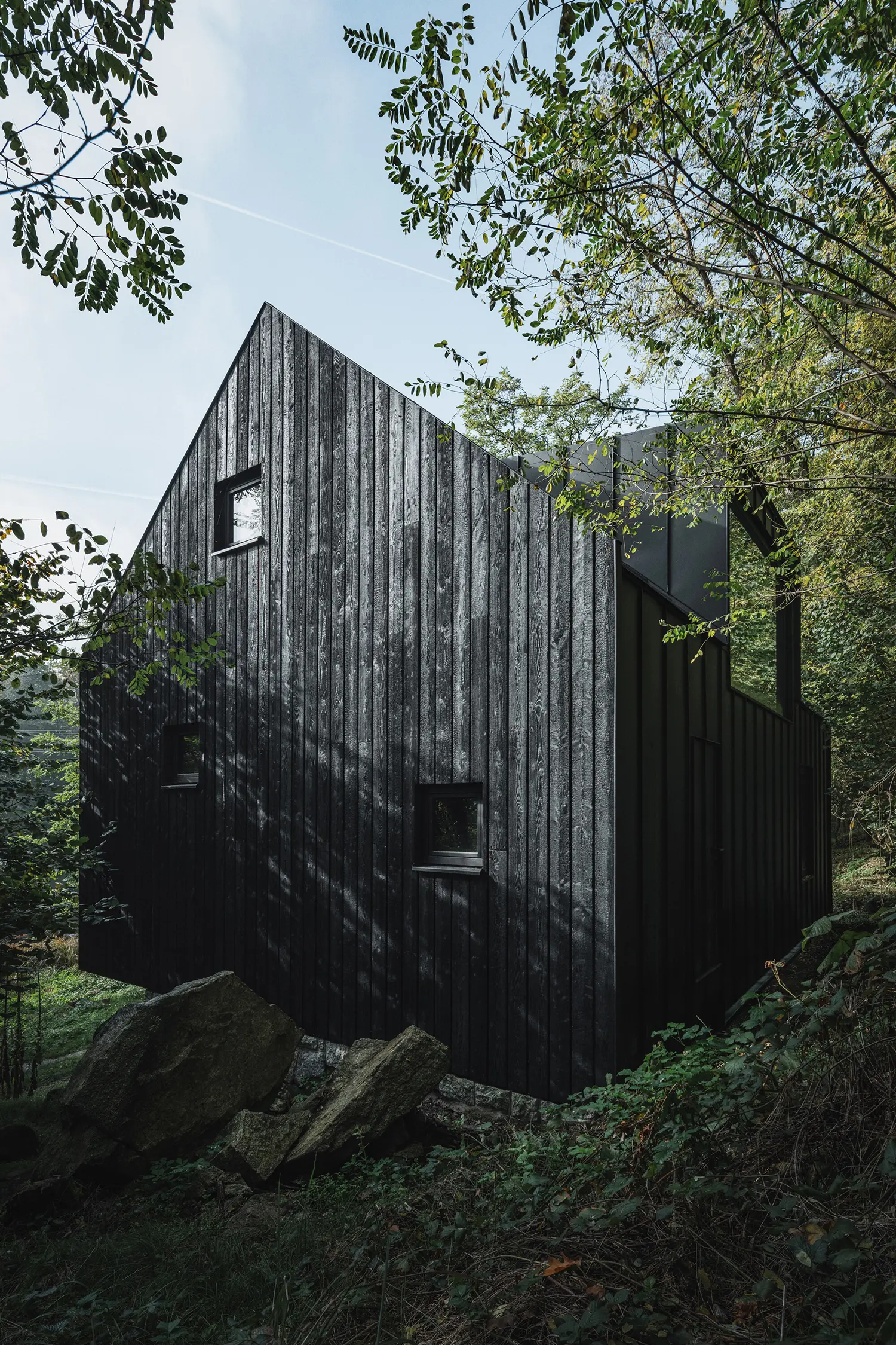 Close-up of the charred larch wood cladding and gable roof of the cabin near large boulders.