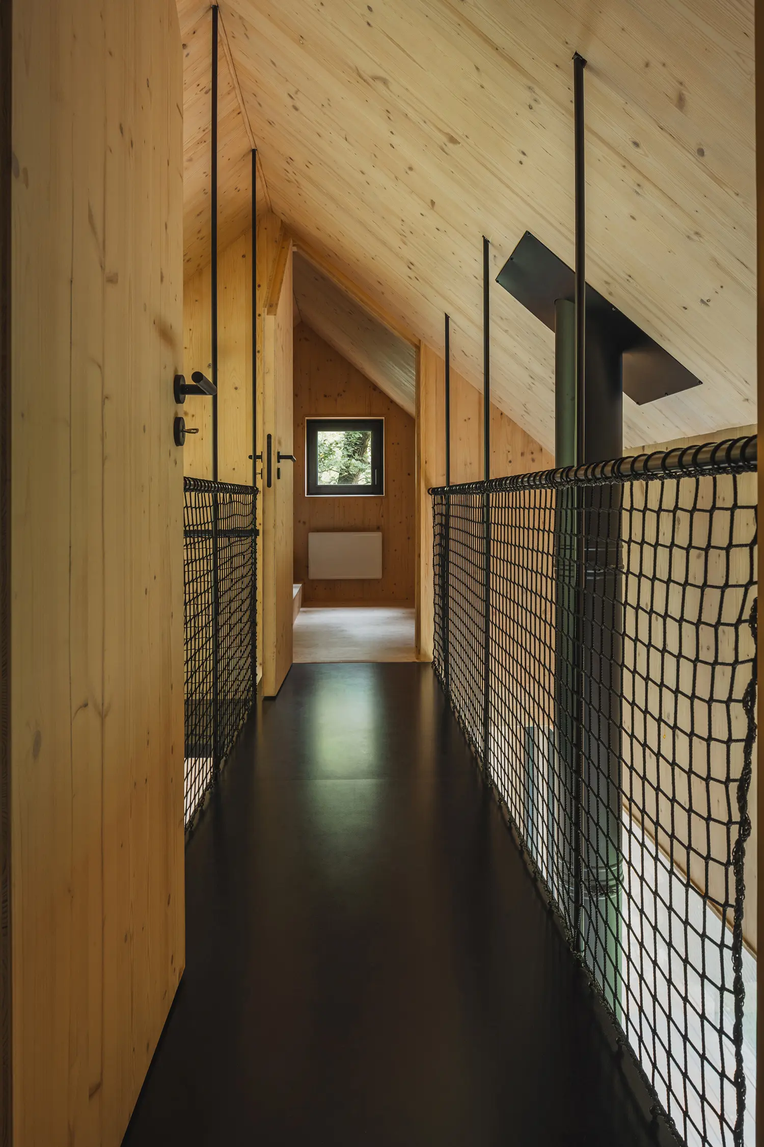 A narrow black catwalk bridge inside the cabin with safety netting, leading toward a small attic window.