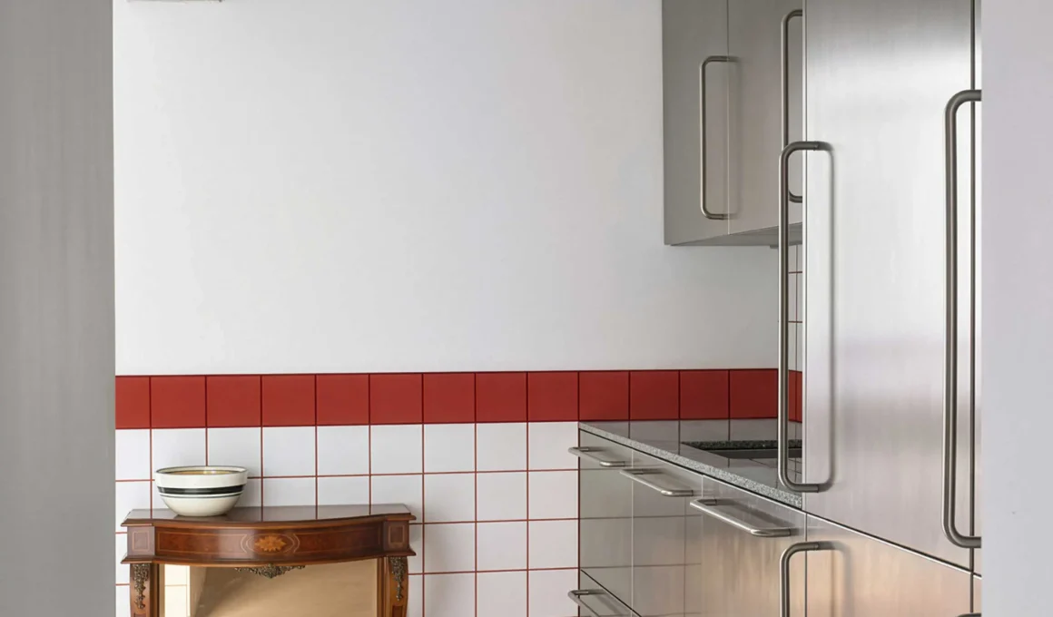 Stainless steel kitchen cabinets against a white and red tiled wall with a vintage wooden console.