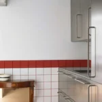 Stainless steel kitchen cabinets against a white and red tiled wall with a vintage wooden console.