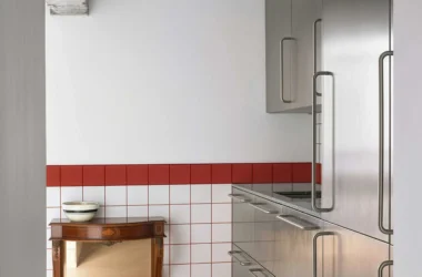 Stainless steel kitchen cabinets against a white and red tiled wall with a vintage wooden console.