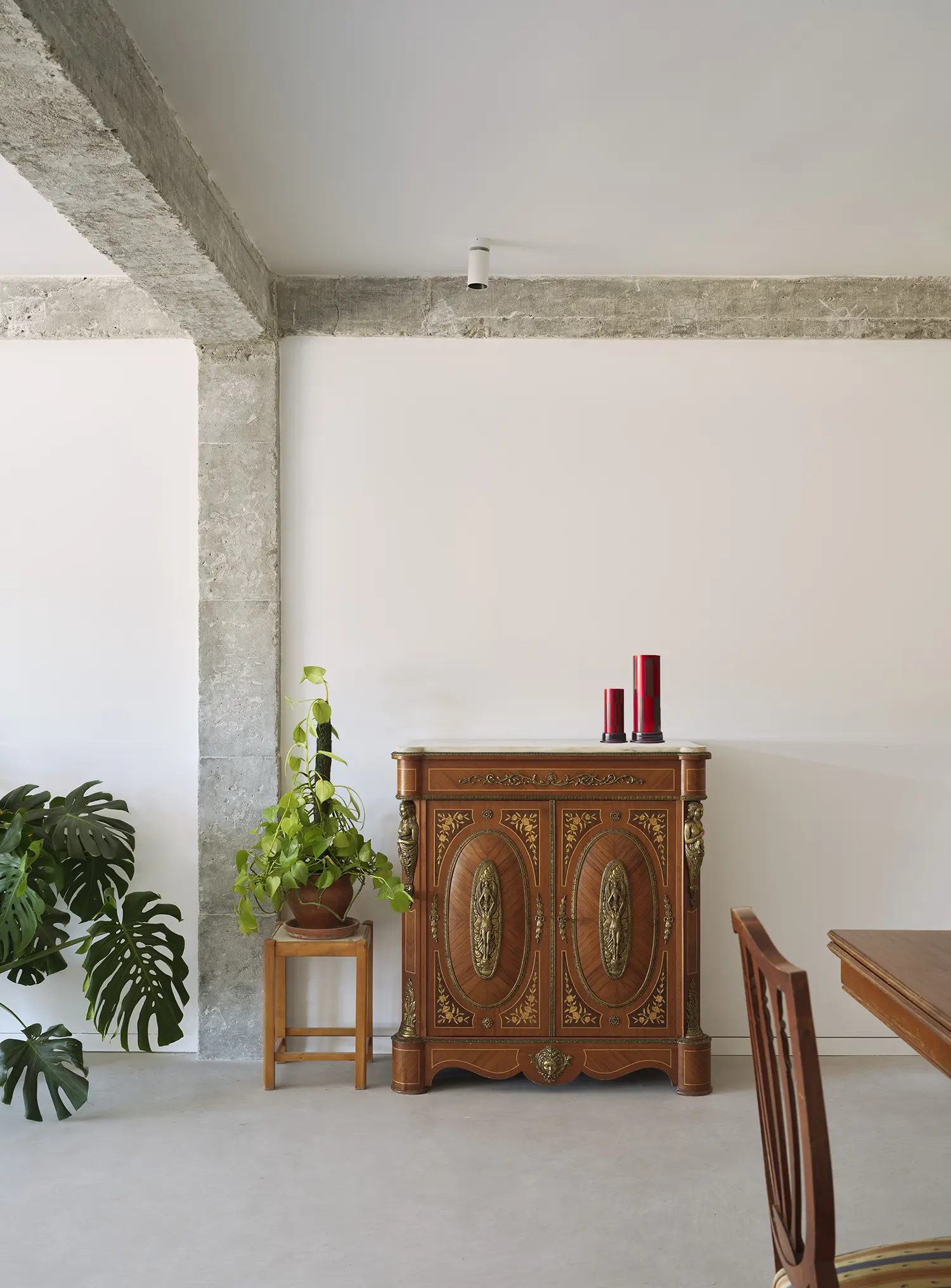 Antique wooden cabinet with ornate carvings standing against a white wall next to a concrete column.