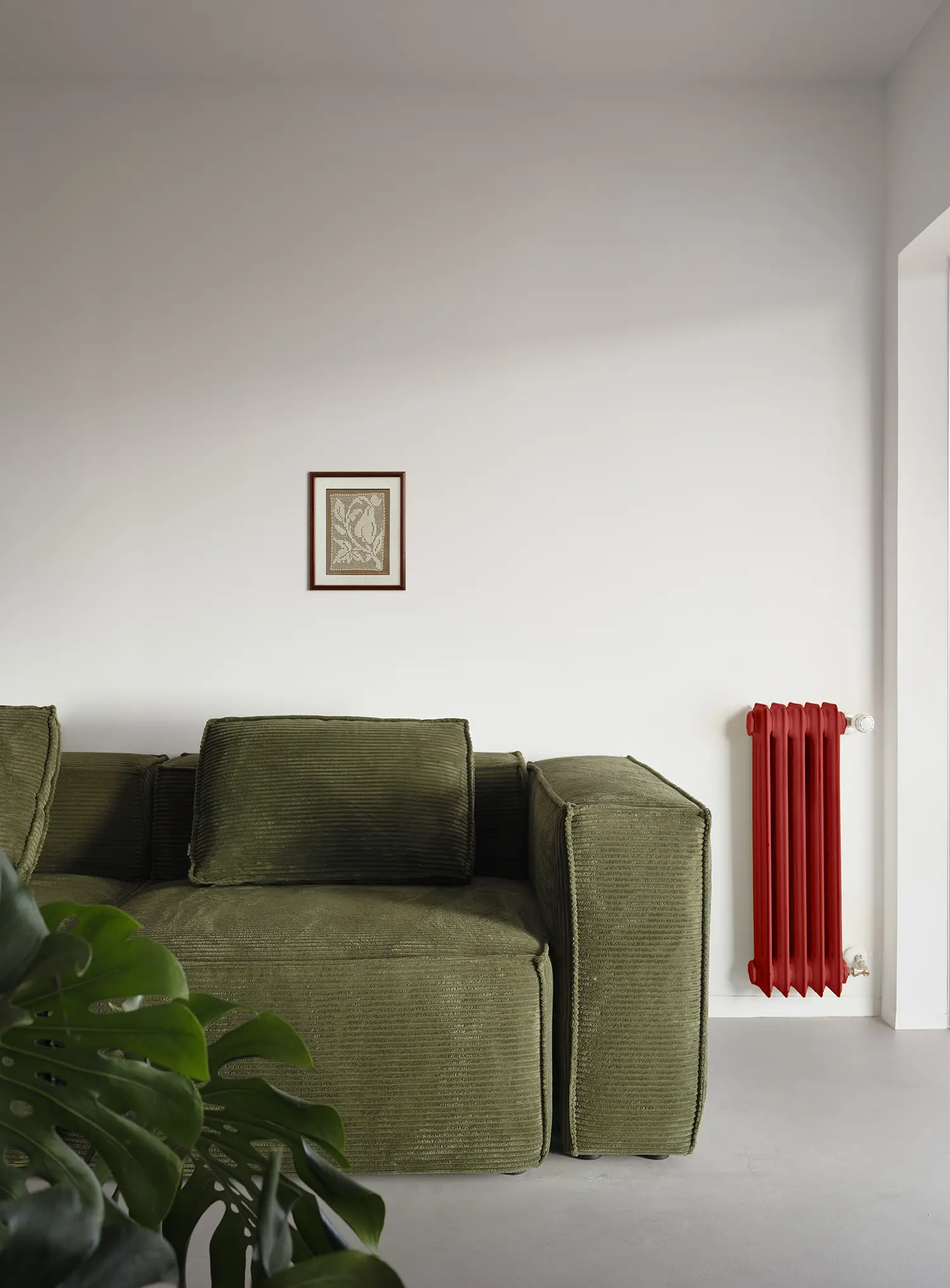 Green corduroy sofa next to a vibrant red cast iron radiator and a white wall with a small framed artwork.