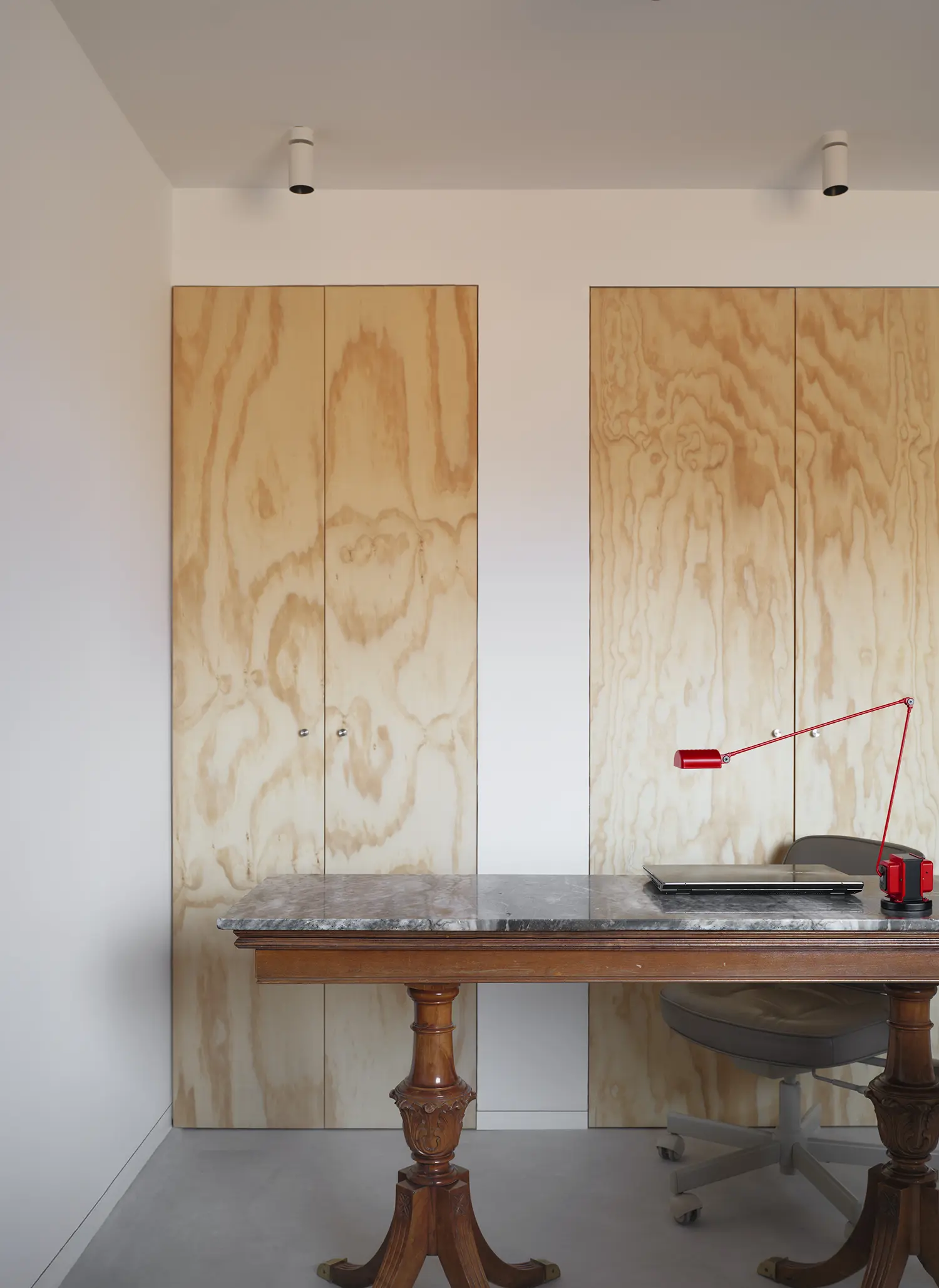 Marble-topped vintage desk with a modern red lamp in front of plywood wardrobe doors.