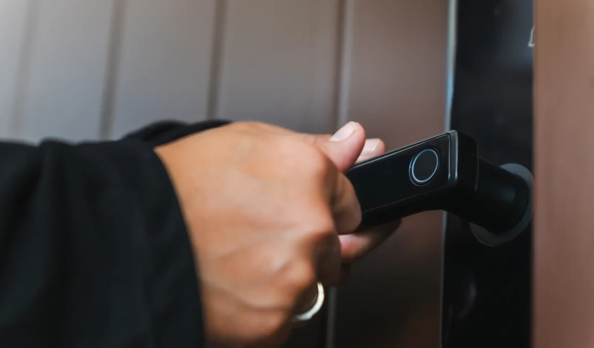Close-up of a person's hand using a biometric fingerprint scanner on a modern black smart door lock handle. Secure entry system.