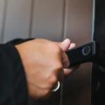 Close-up of a person's hand using a biometric fingerprint scanner on a modern black smart door lock handle. Secure entry system.