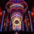 Symmetrical wide interior shot of Église Saint-Roch featuring vaulted ceilings outlined in pink, orange, and blue light.