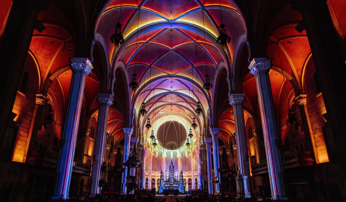 Symmetrical wide interior shot of Église Saint-Roch featuring vaulted ceilings outlined in pink, orange, and blue light.