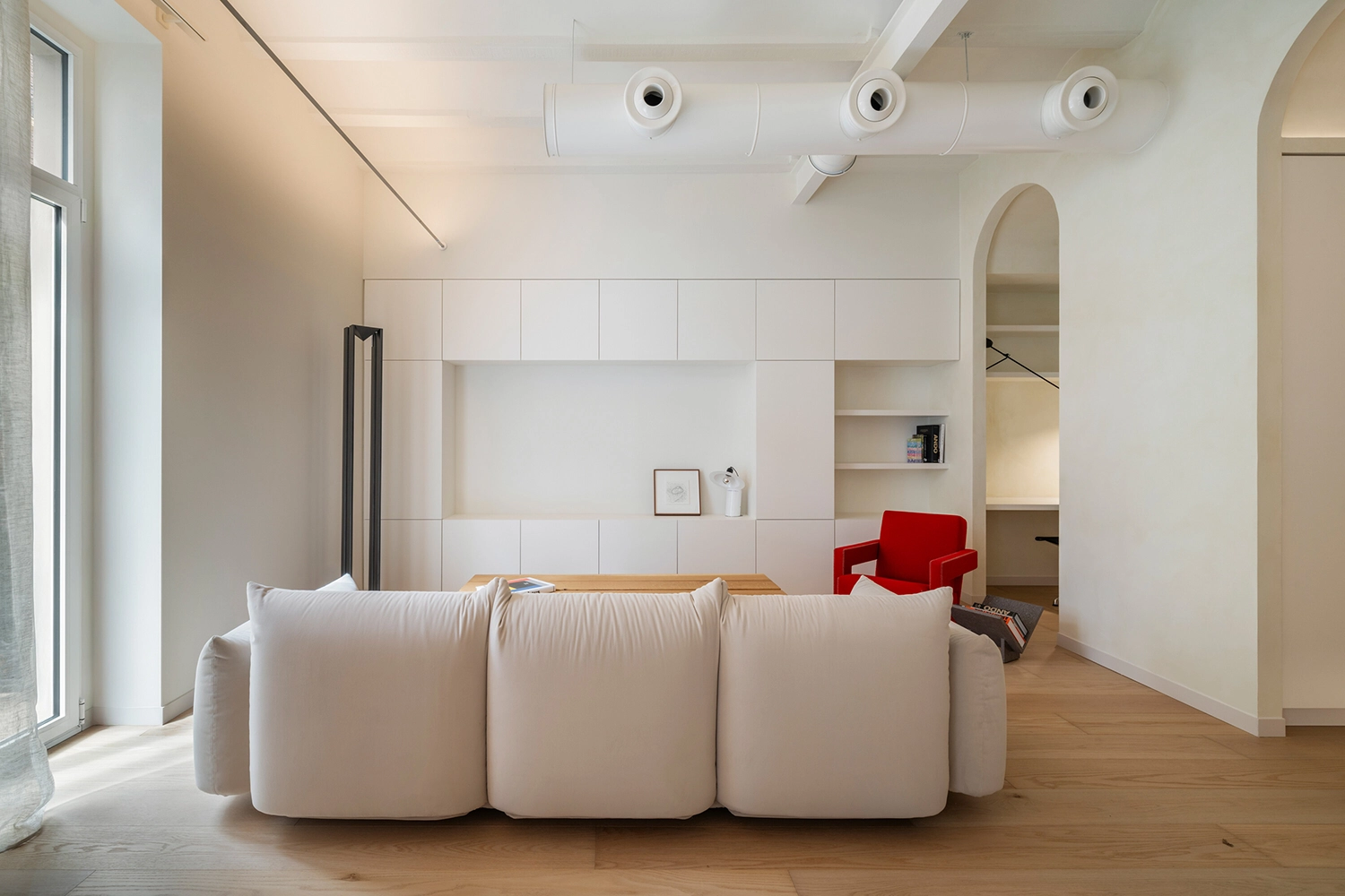 Minimalist white living room with a cream sofa, white cabinetry, and a single red armchair in a Spanish home.