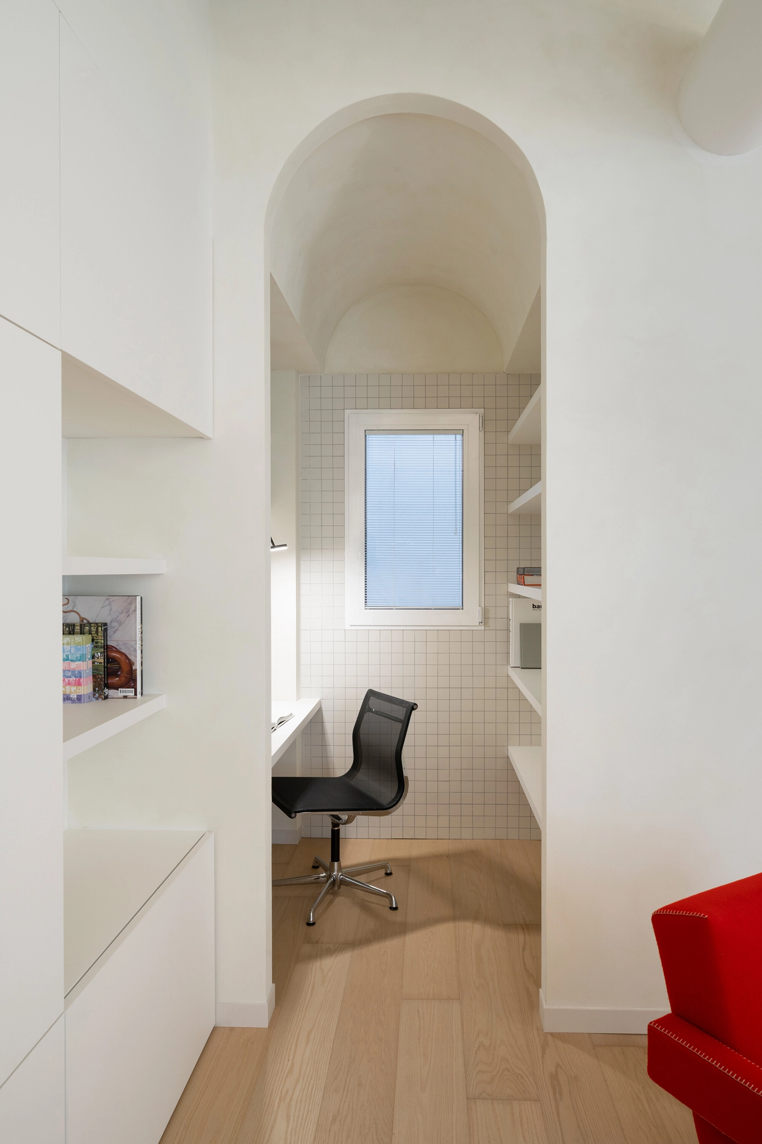 A narrow workspace tucked into an arched niche with white square tiles and built-in shelving.