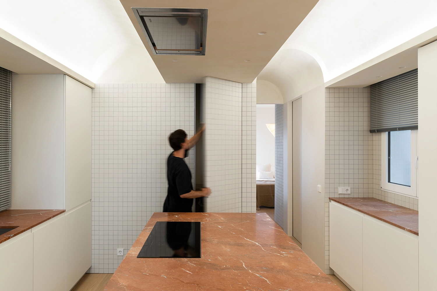 Person moving through a white tiled kitchen with Red Alicante marble countertops and vaulted ceilings.