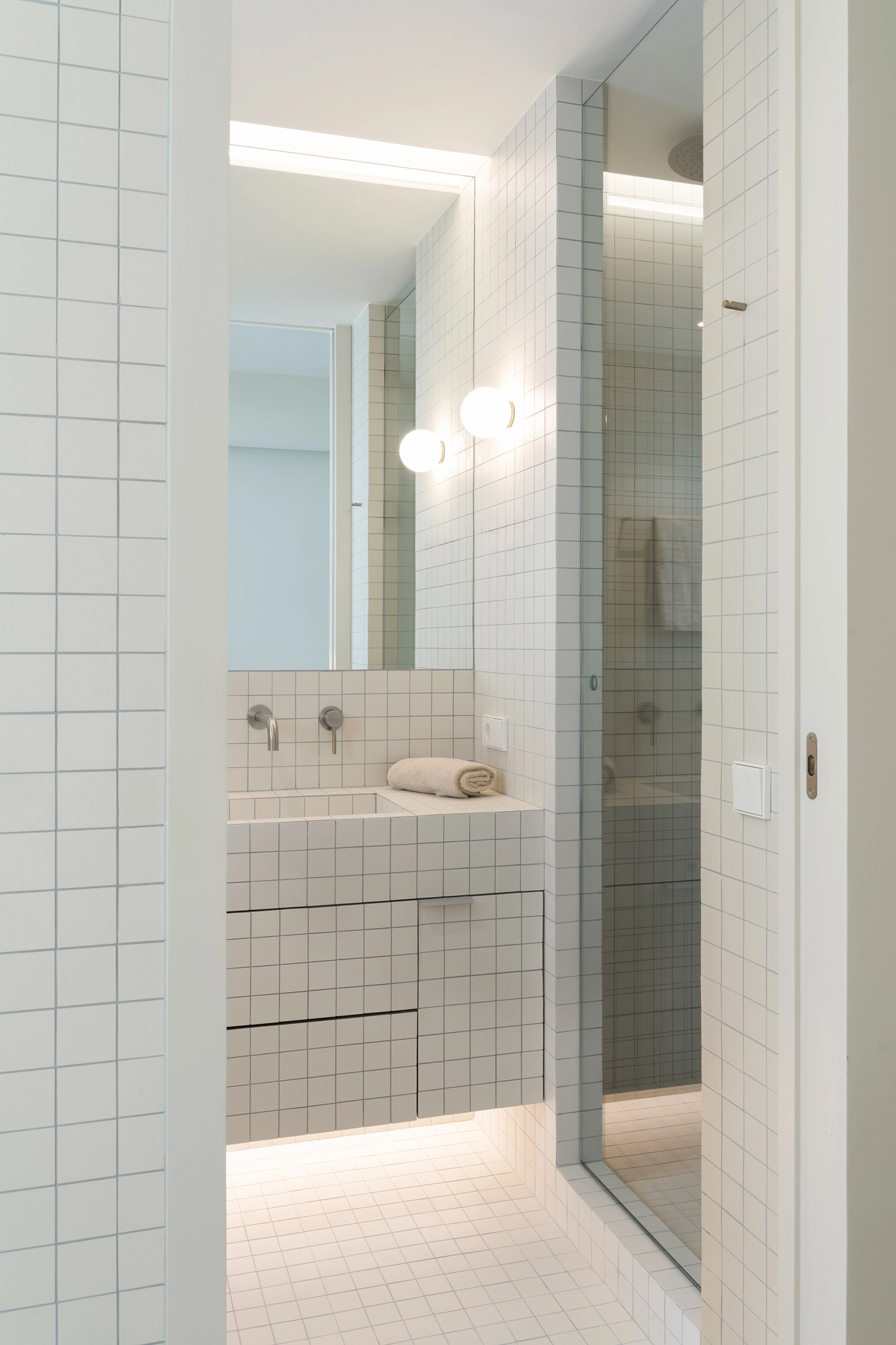 Modern bathroom featuring a custom washbasin and walls entirely clad in 6x6 cm white square tiles.