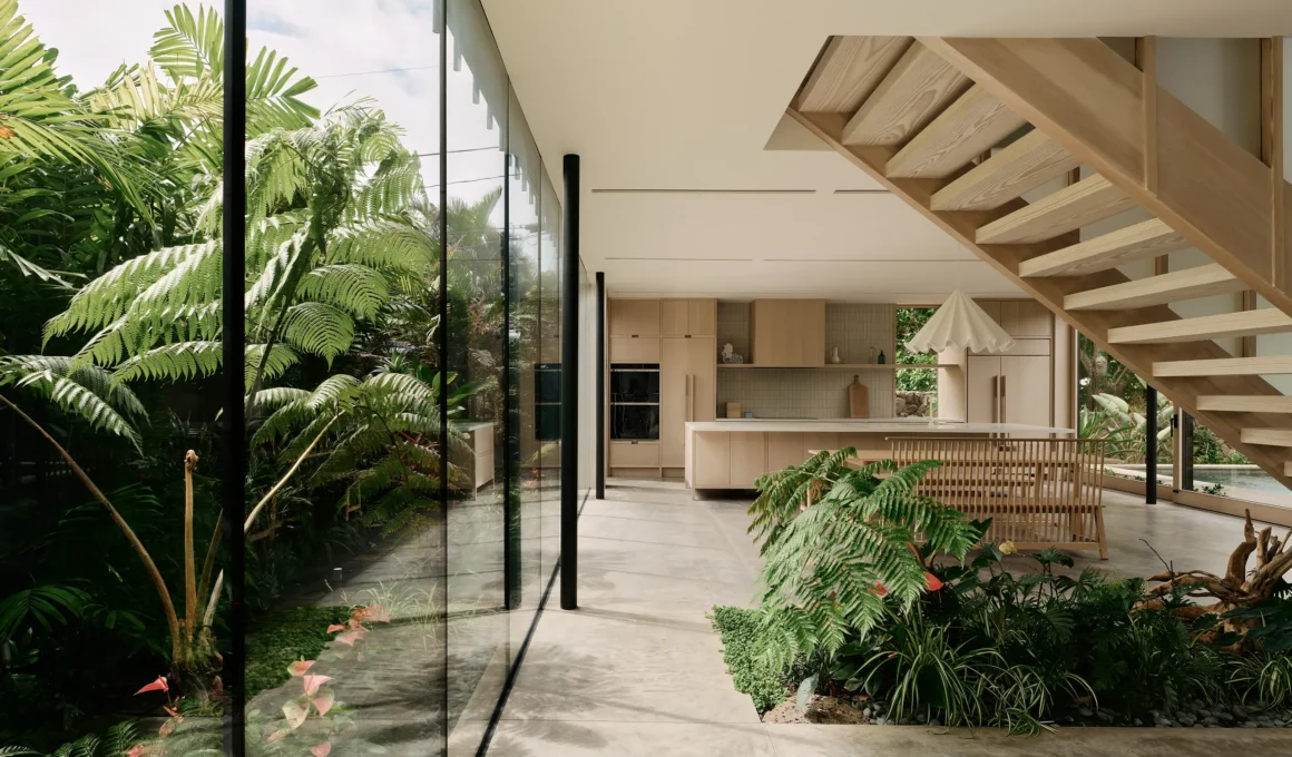 Indoor-outdoor living space with floor-to-ceiling glass walls and lush tropical greenery.