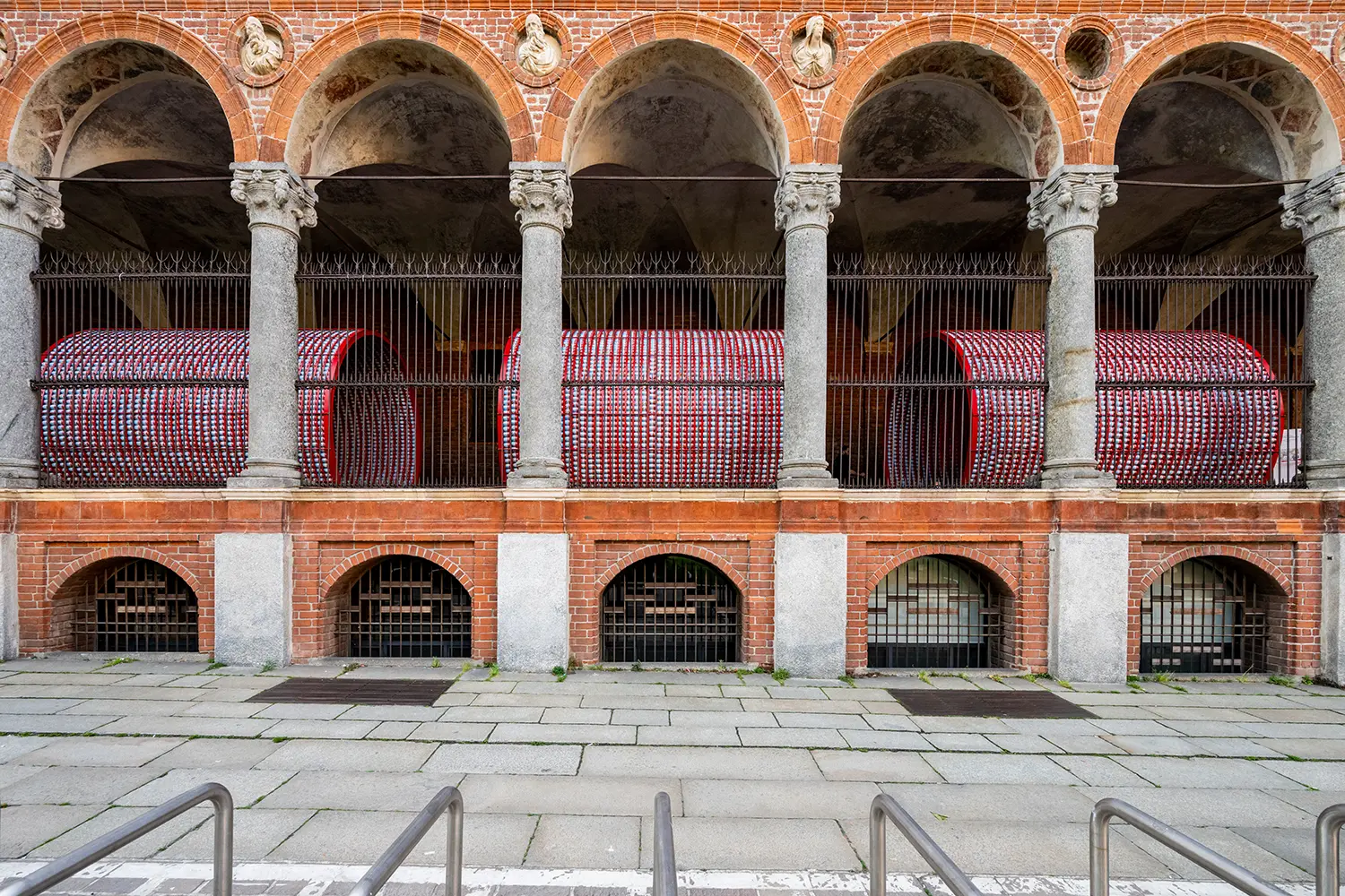 Exterior view of the installation seen through a wrought iron fence and classical stone arches.
