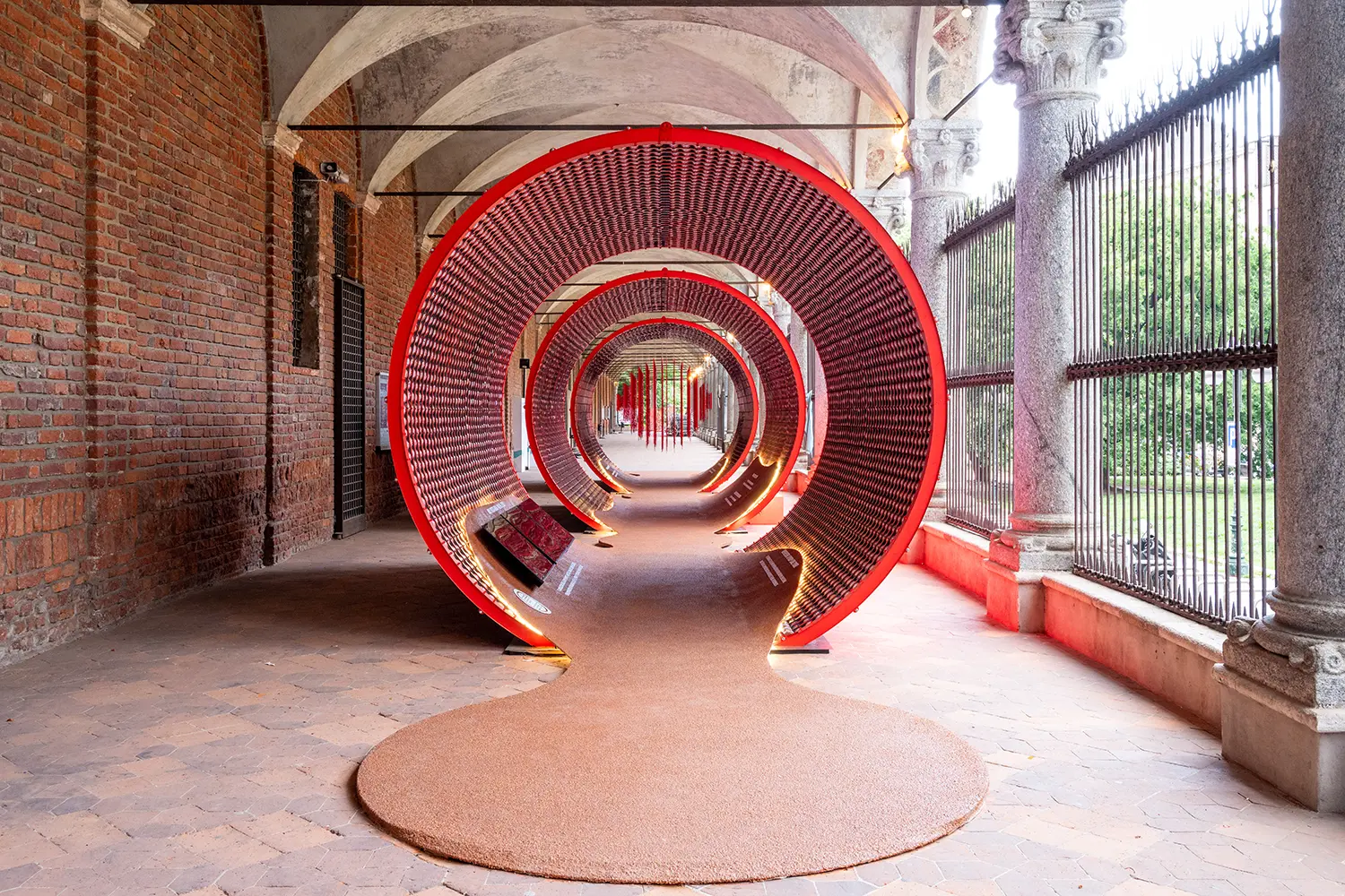 Long perspective view through a series of red circular tunnels under a brick and stone portico.