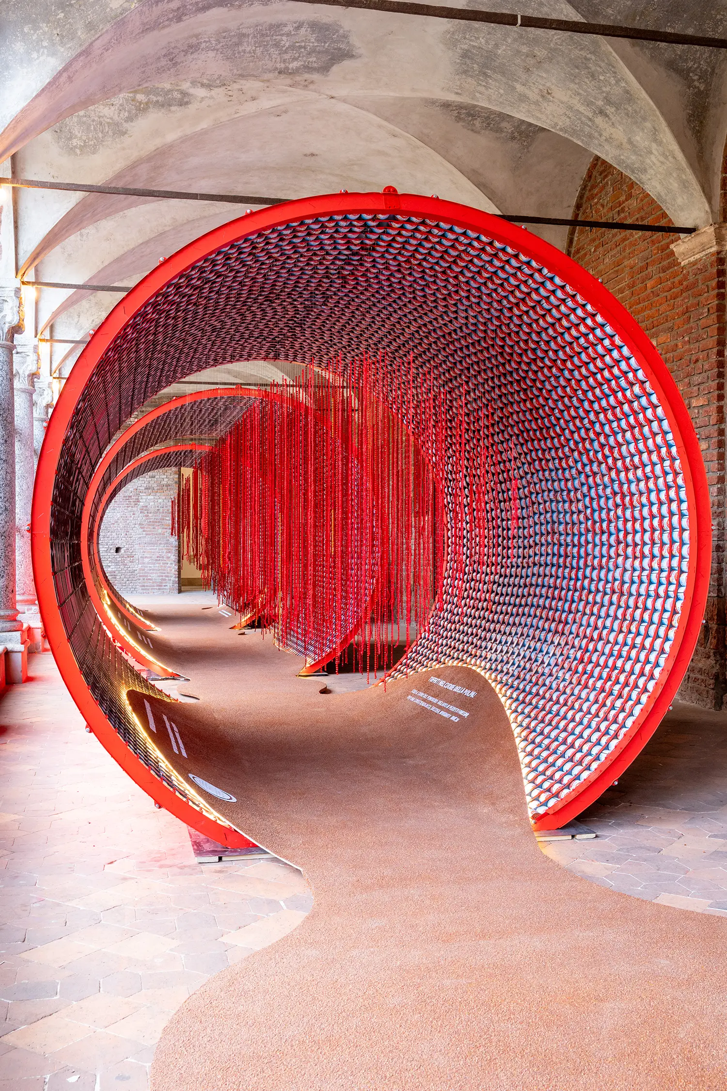 Perspective view through red tunnels featuring thousands of hanging red vertical strands in the center.