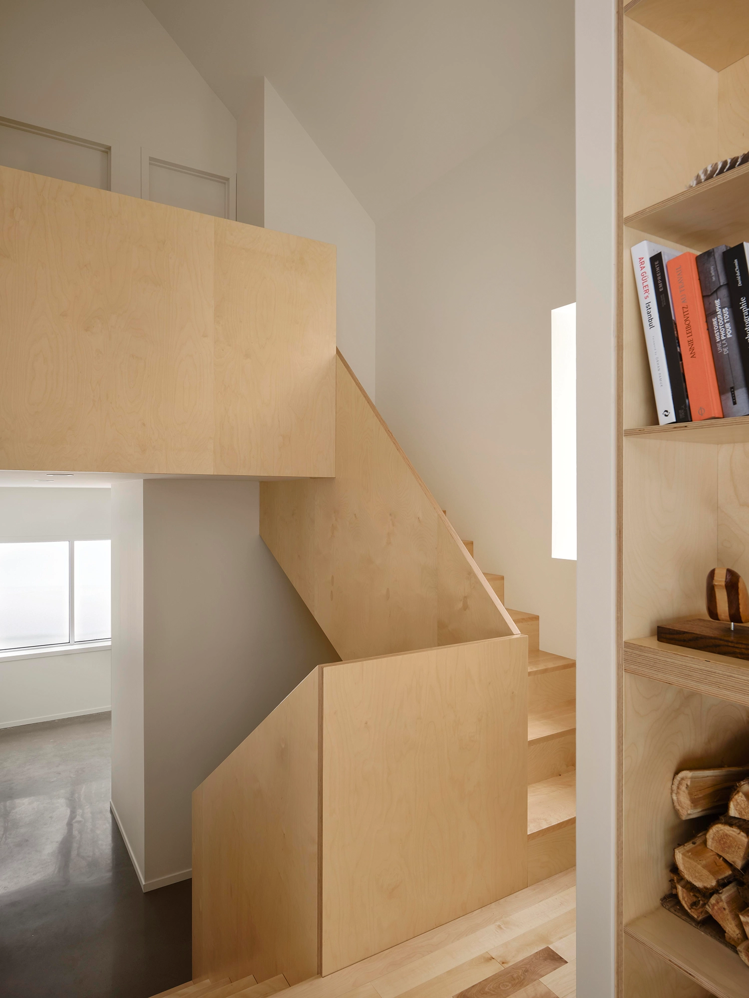 Interior view of a light-colored plywood staircase and integrated shelving unit in a modern cabin.