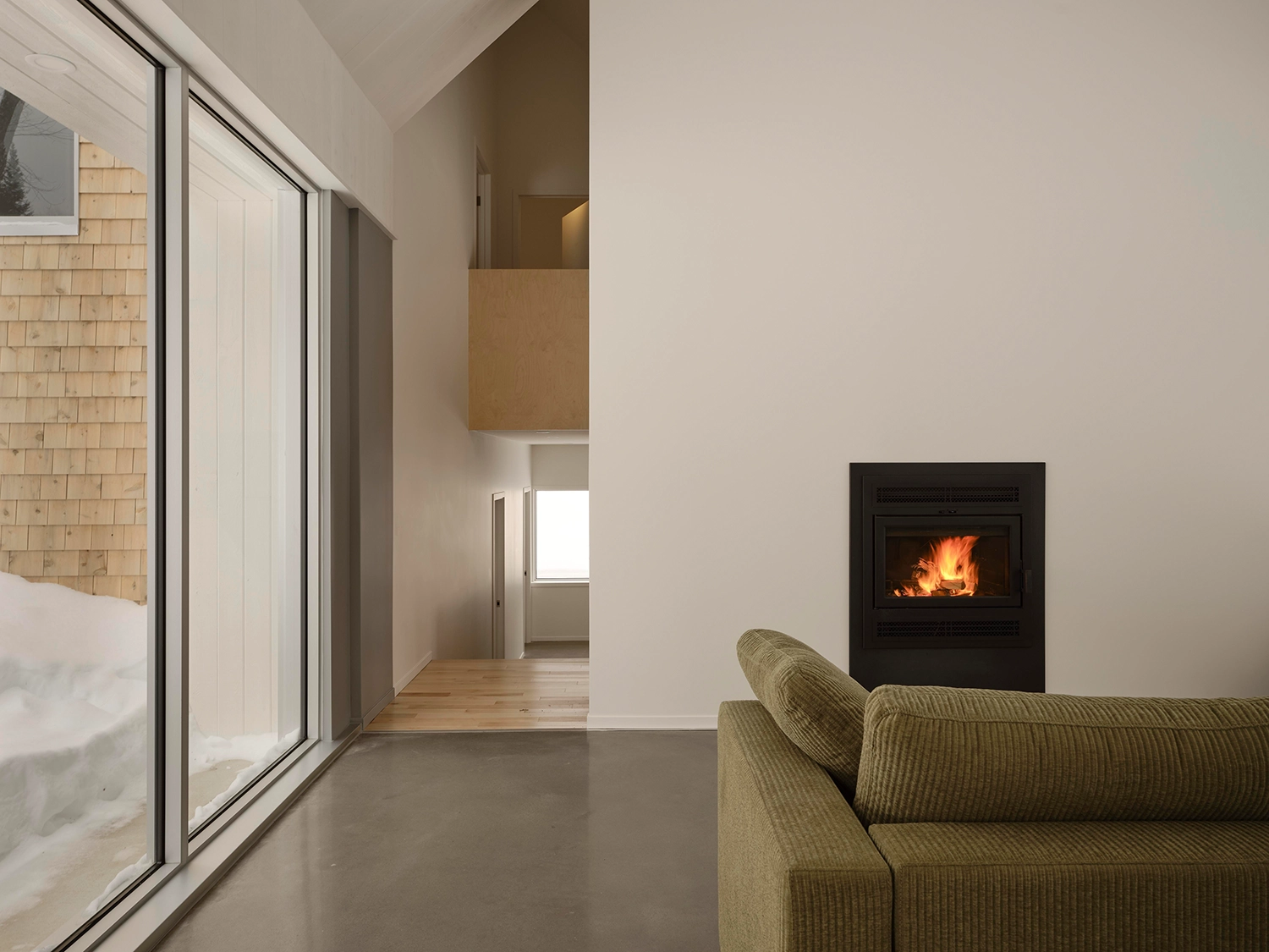 Modern living room featuring a black built-in fireplace and a green textured sofa with forest views.