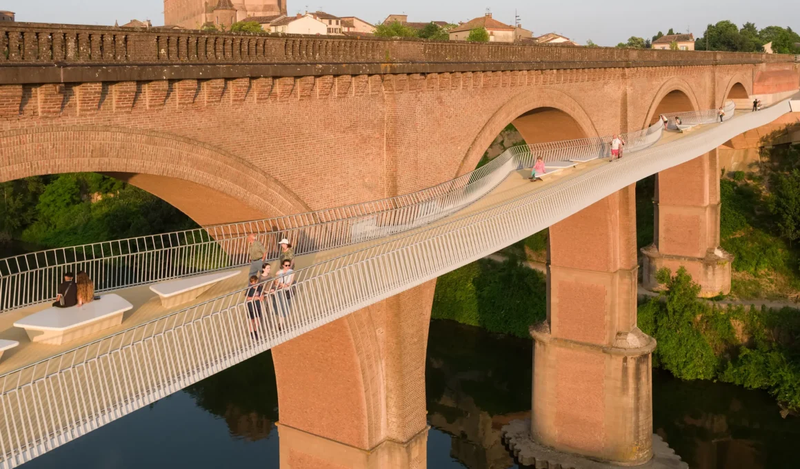 Close-up of the steel cantilevered footbridge with integrated benches and pedestrians, attached to the masonry railway viaduct in Albi.