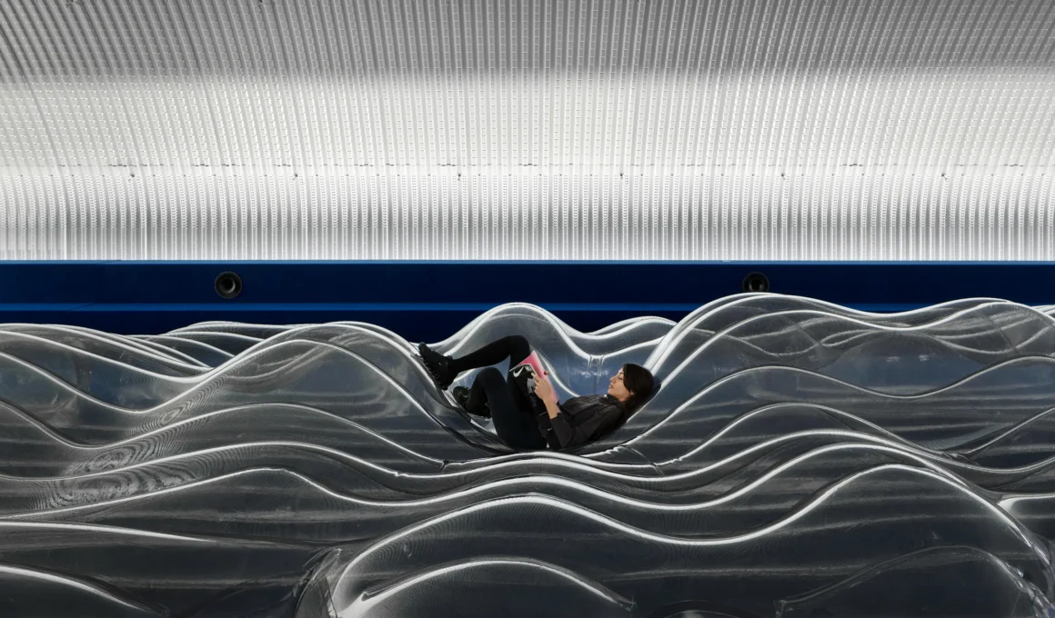 A visitor lying on a large, wave-like transparent inflatable installation inside a vaulted tunnel at NikeAir_Lab.
