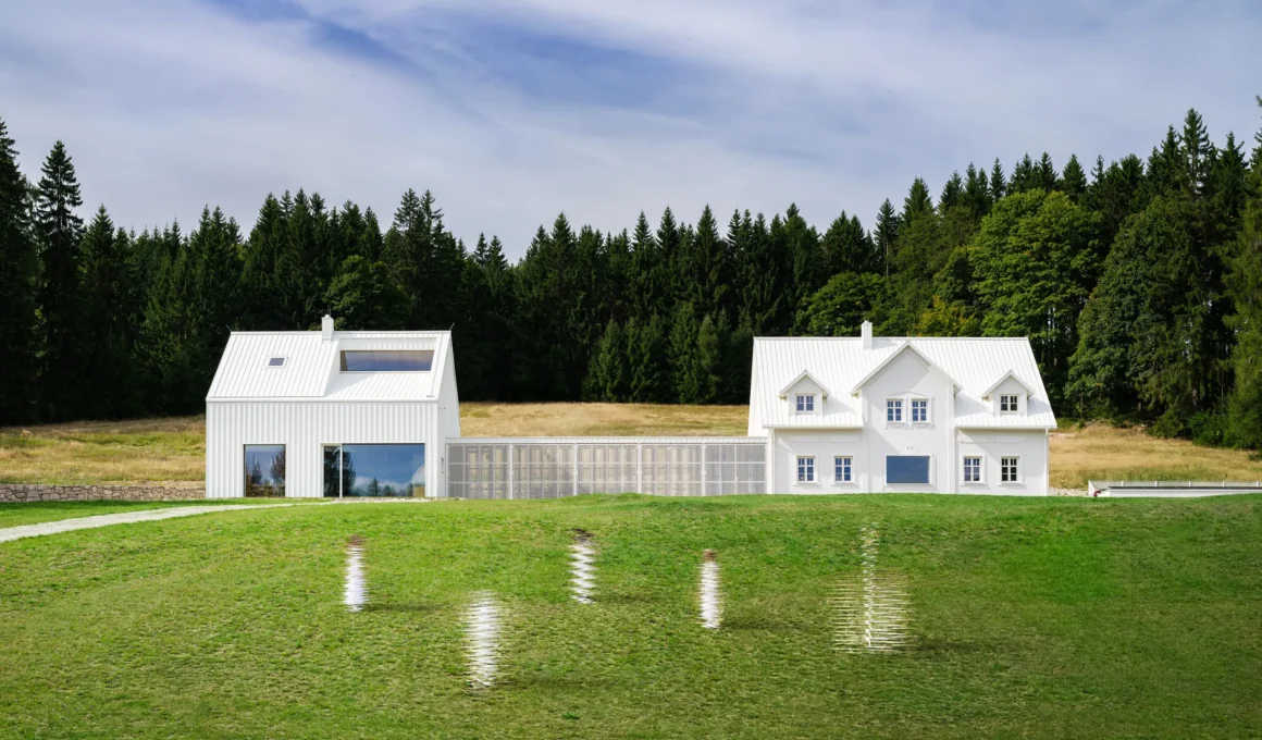 Exterior view of a white modern homestead in the Ore Mountains with two gabled volumes connected by a wooden slatted corridor.
