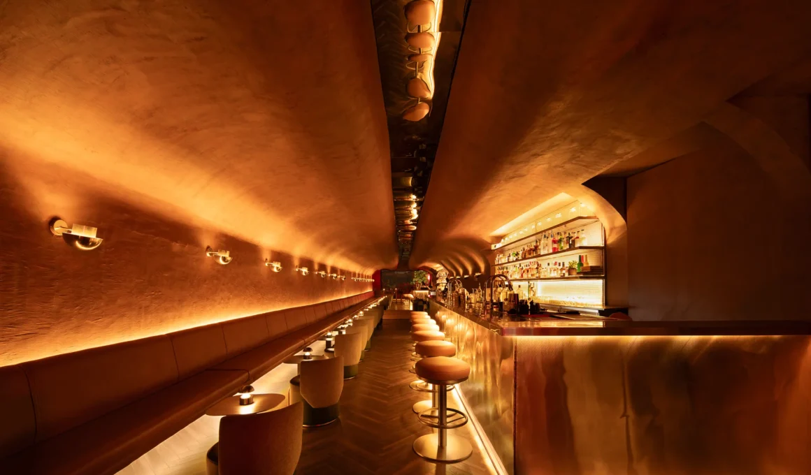 Wide view of the tubular No Vacancy bar interior in New Delhi by Studiio Dangg featuring a long leather bench and glowing stainless steel bar.