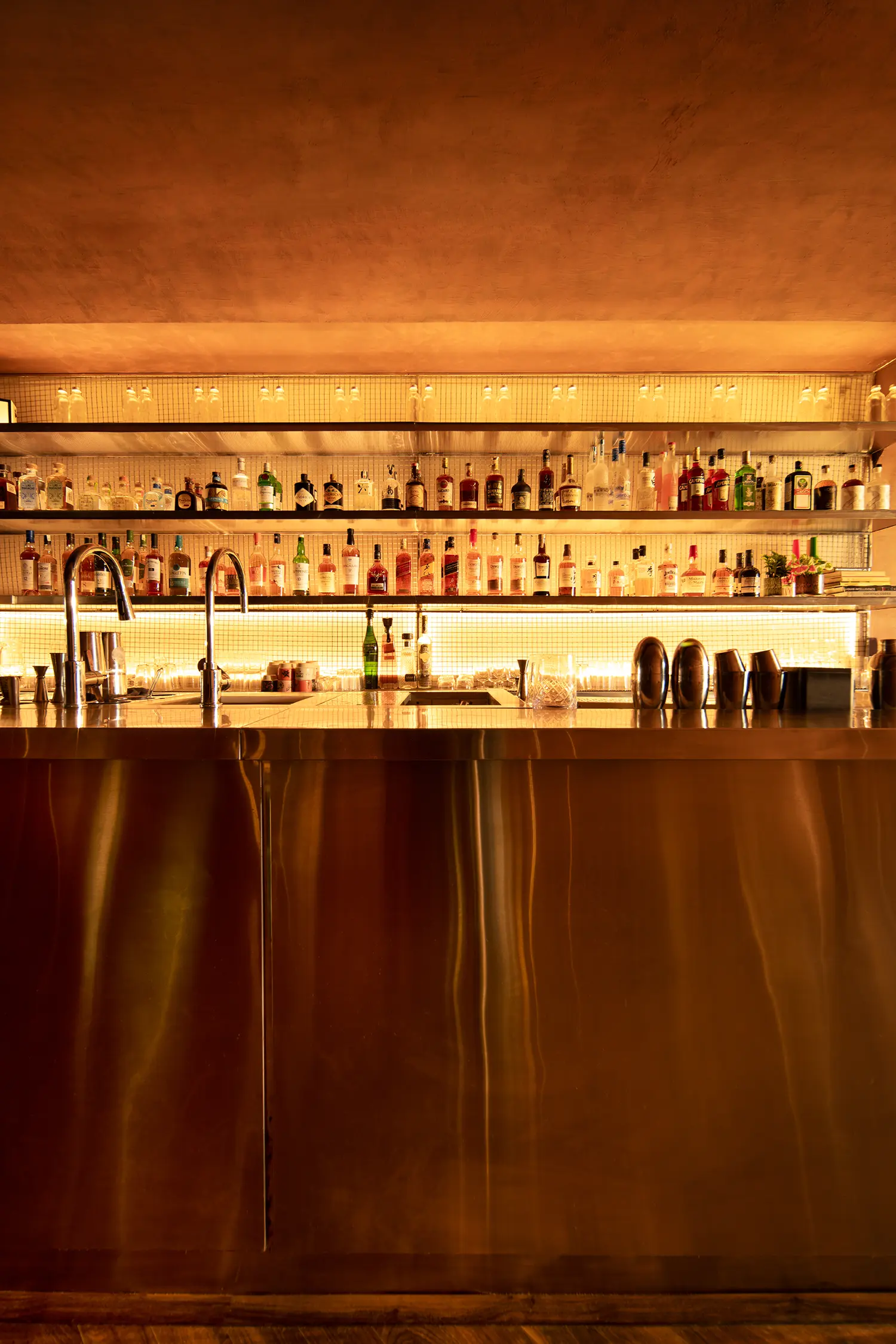 Frontal view of the stainless steel bar back at No Vacancy featuring tiered shelving and glowing mesh.