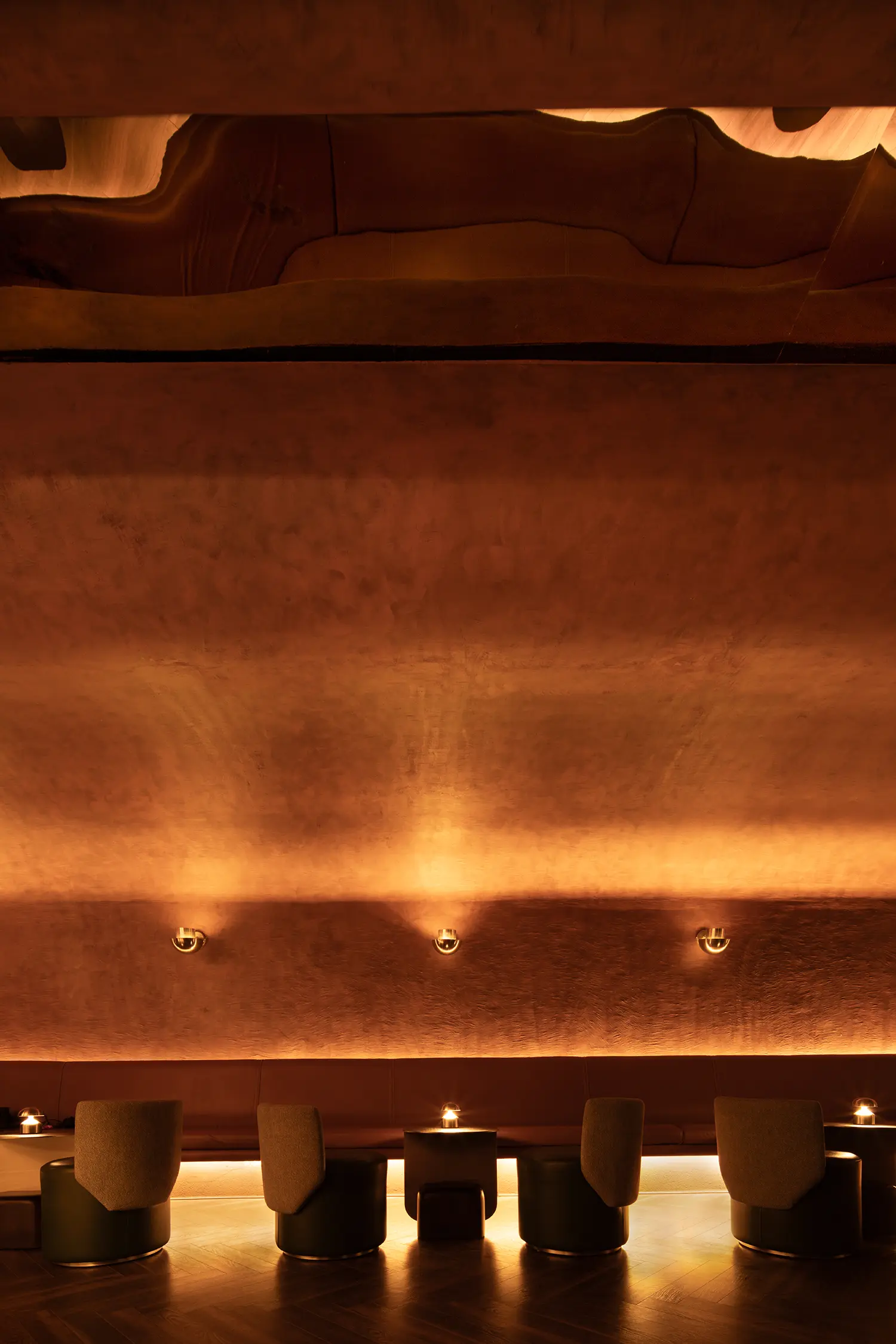 Vertical shot of curved, earth-toned walls and minimalist wall sconces at No Vacancy.