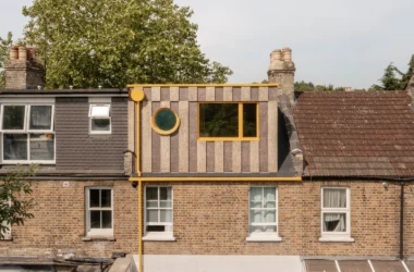 Exterior view of a Victorian terrace roof featuring a multi-tonal cork loft extension with yellow circular and rectangular windows.