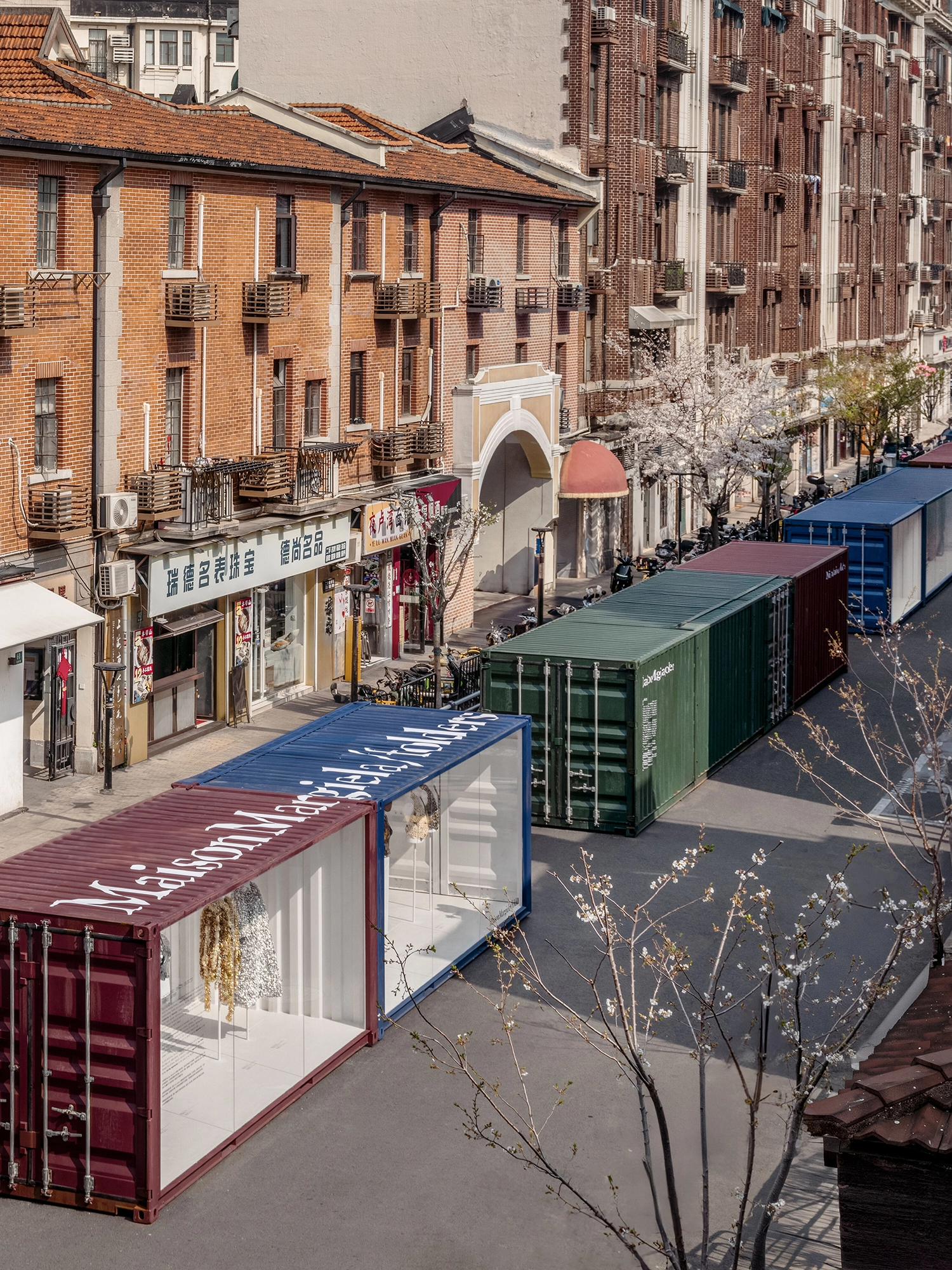 High-angle view of colorful shipping containers placed on a narrow street in Shanghai between traditional brick buildings.