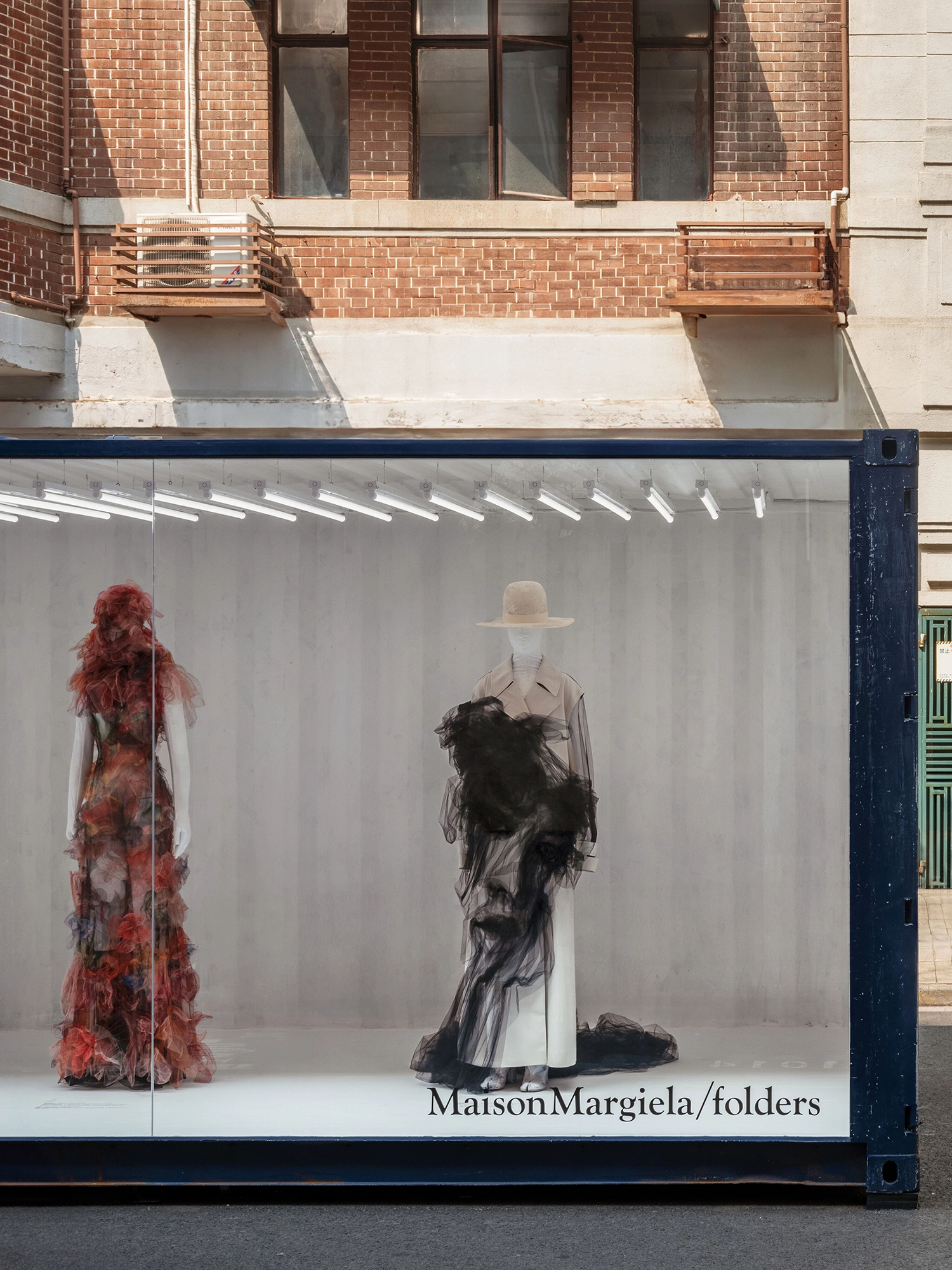 Frontal view of a dark blue shipping container featuring a Maison Margiela logo and two avant-garde mannequins.