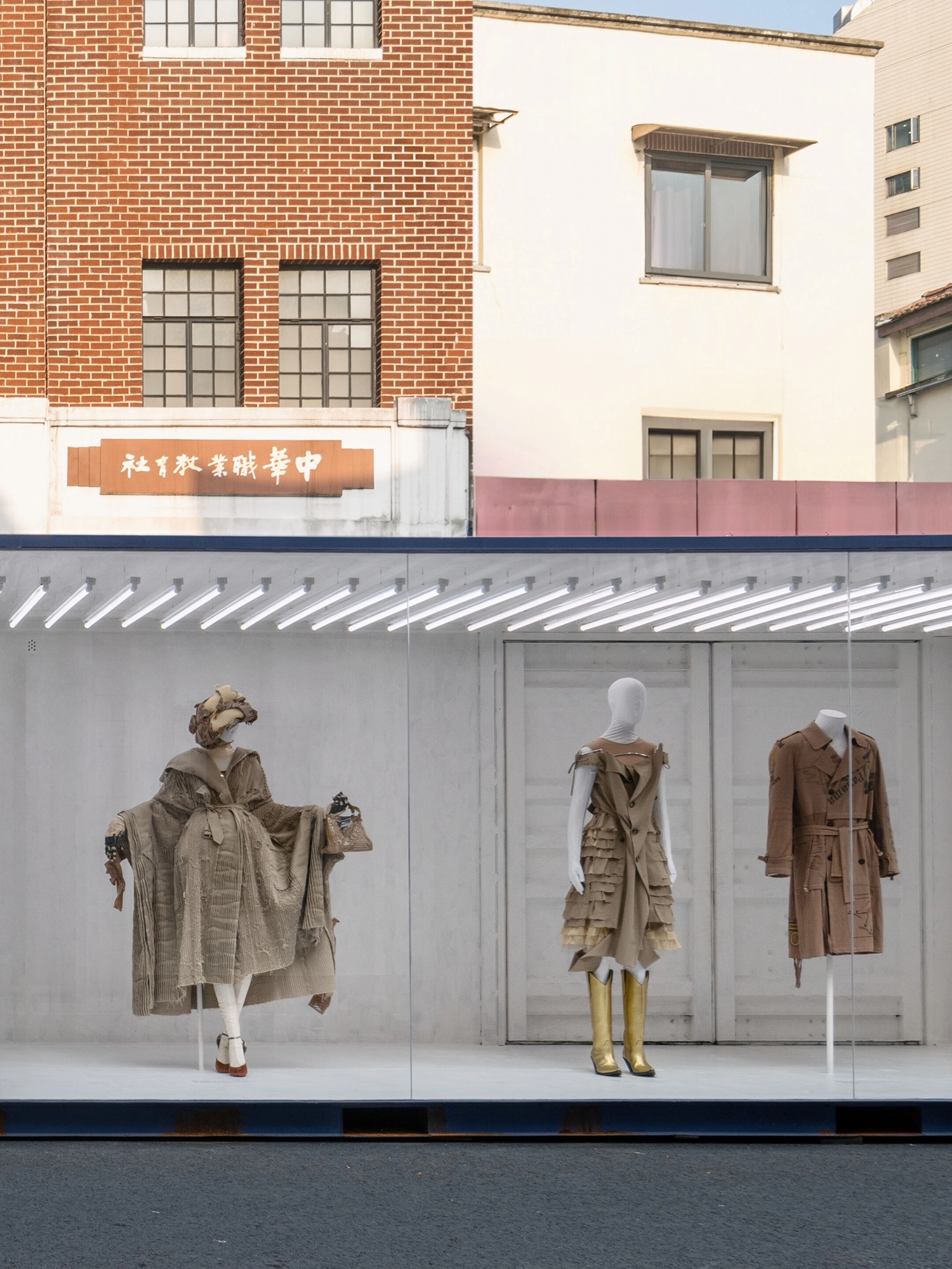 Three mannequins showcasing Maison Margiela's deconstructed trench coats inside a white container under bright lights.