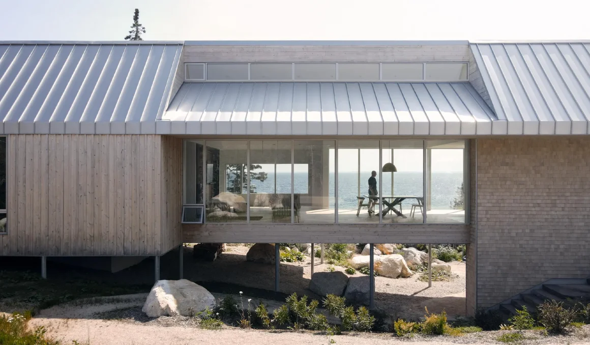 A bridge-like timber house spanning a rocky valley with steel stilts and a metal gable roof in Nova Scotia.