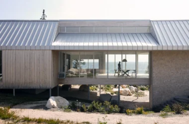 A bridge-like timber house spanning a rocky valley with steel stilts and a metal gable roof in Nova Scotia.