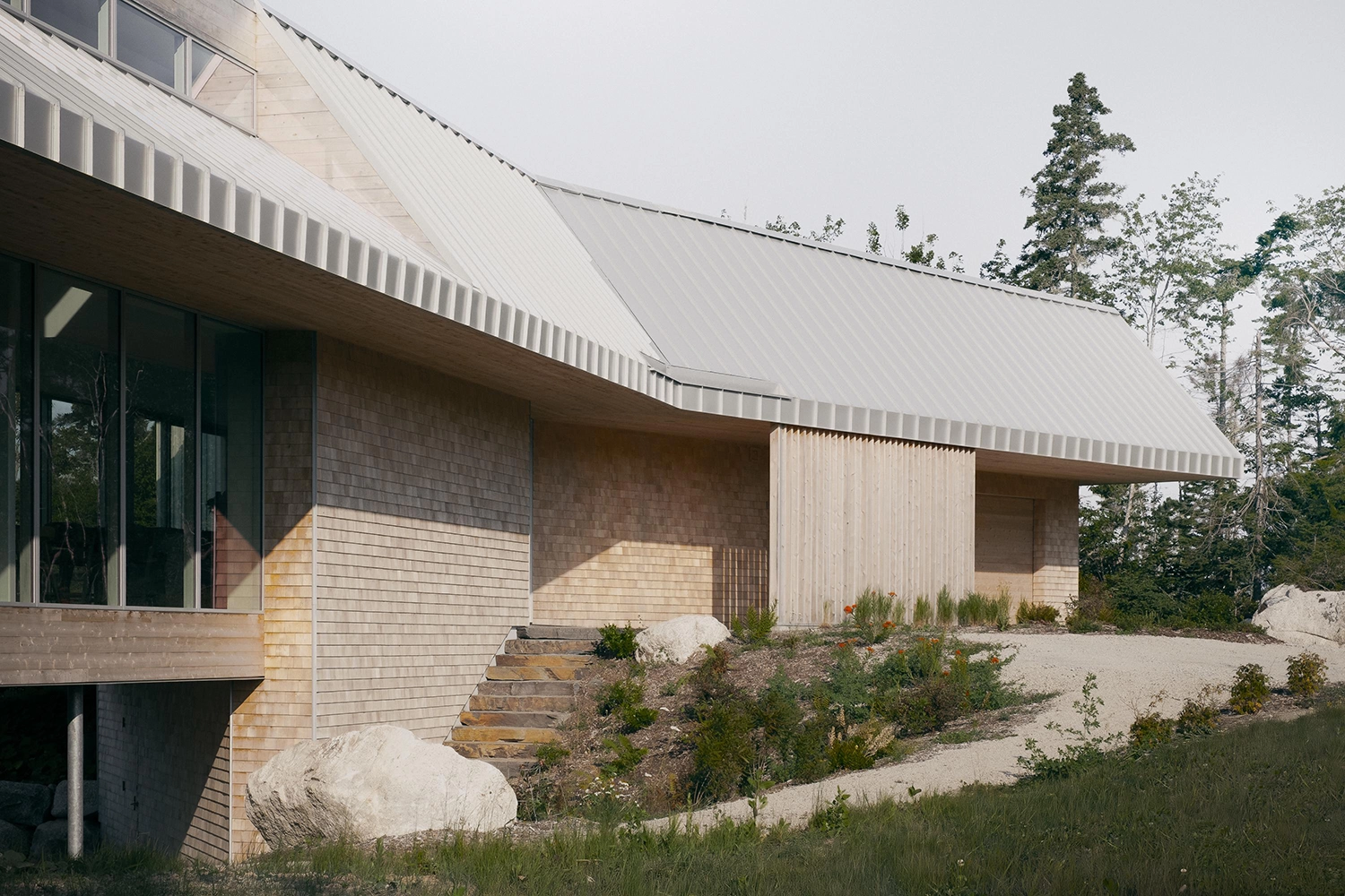 Close-up of cedar shingles and vertical wood cladding meeting a grey metal offset gable roof.