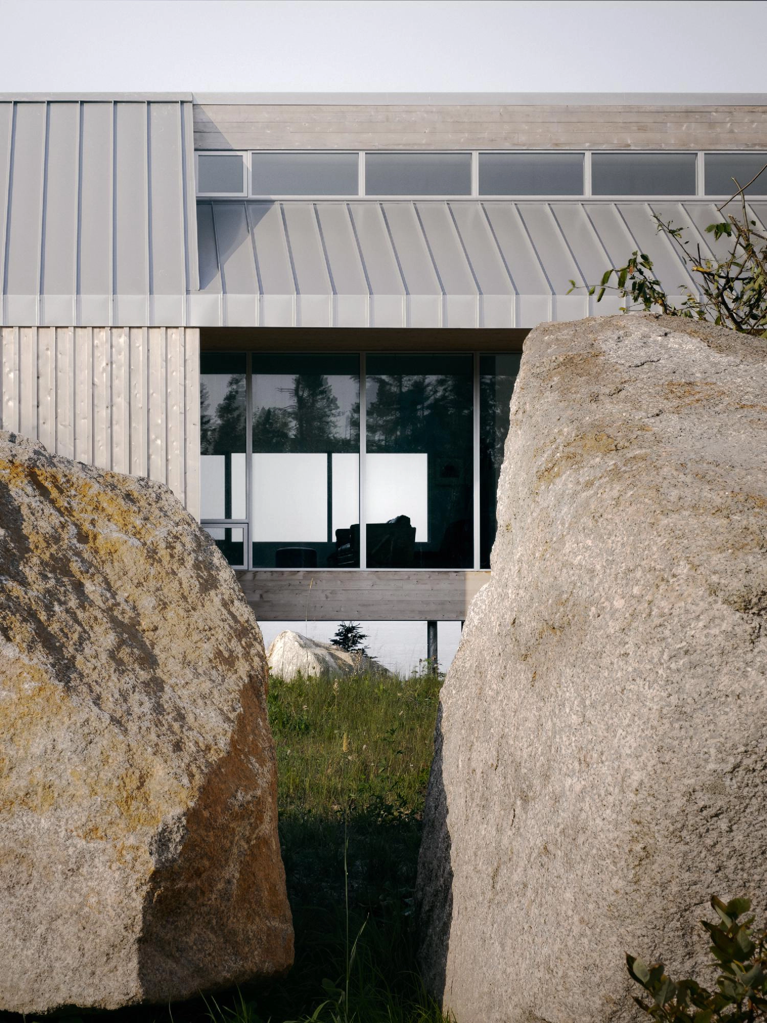 Looking through two large granite boulders toward the glass facade of the East River Residence.