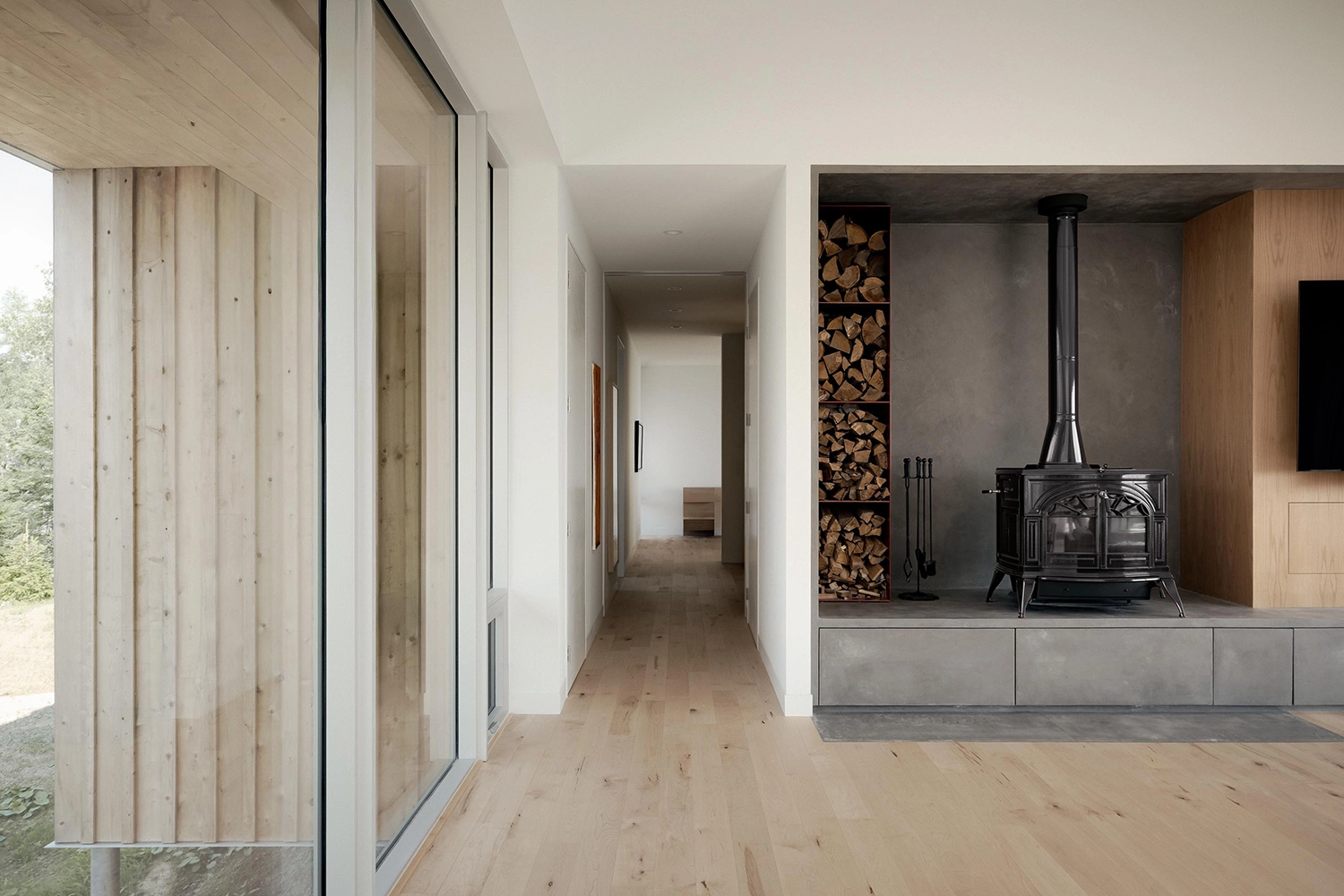 Minimalist interior hallway featuring a concrete hearth, wood-burning stove, and built-in wood storage.