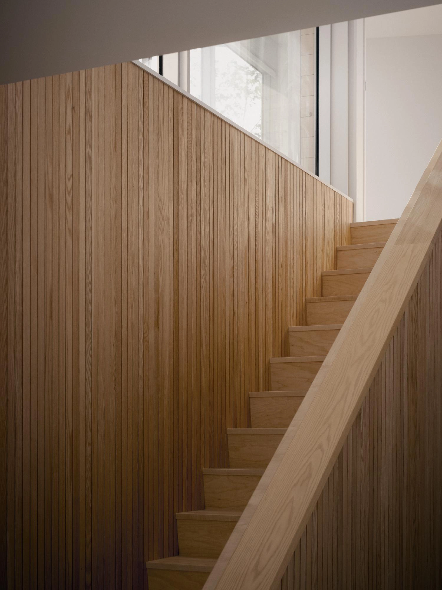 Detail of a wooden staircase with vertical cedar slat wall paneling and a light oak handrail.