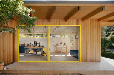 Wide sliding glass doors with yellow frames opening from a wood-clad studio onto a timber deck.