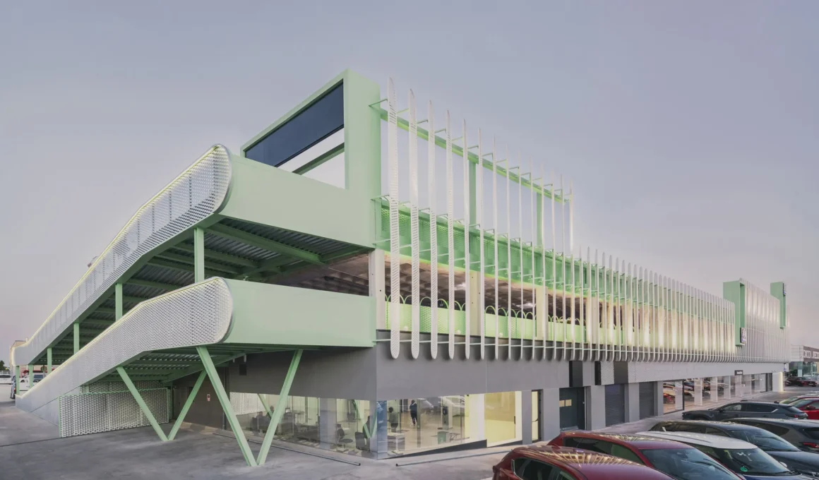 Exterior view of Leganés Auto Center featuring a mint green ramp and perforated metal facade in Madrid.