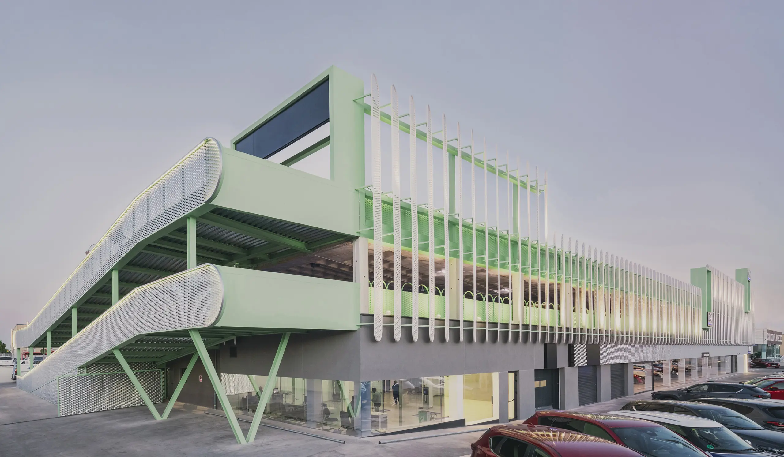Exterior view of Leganés Auto Center featuring a mint green ramp and perforated metal facade in Madrid.