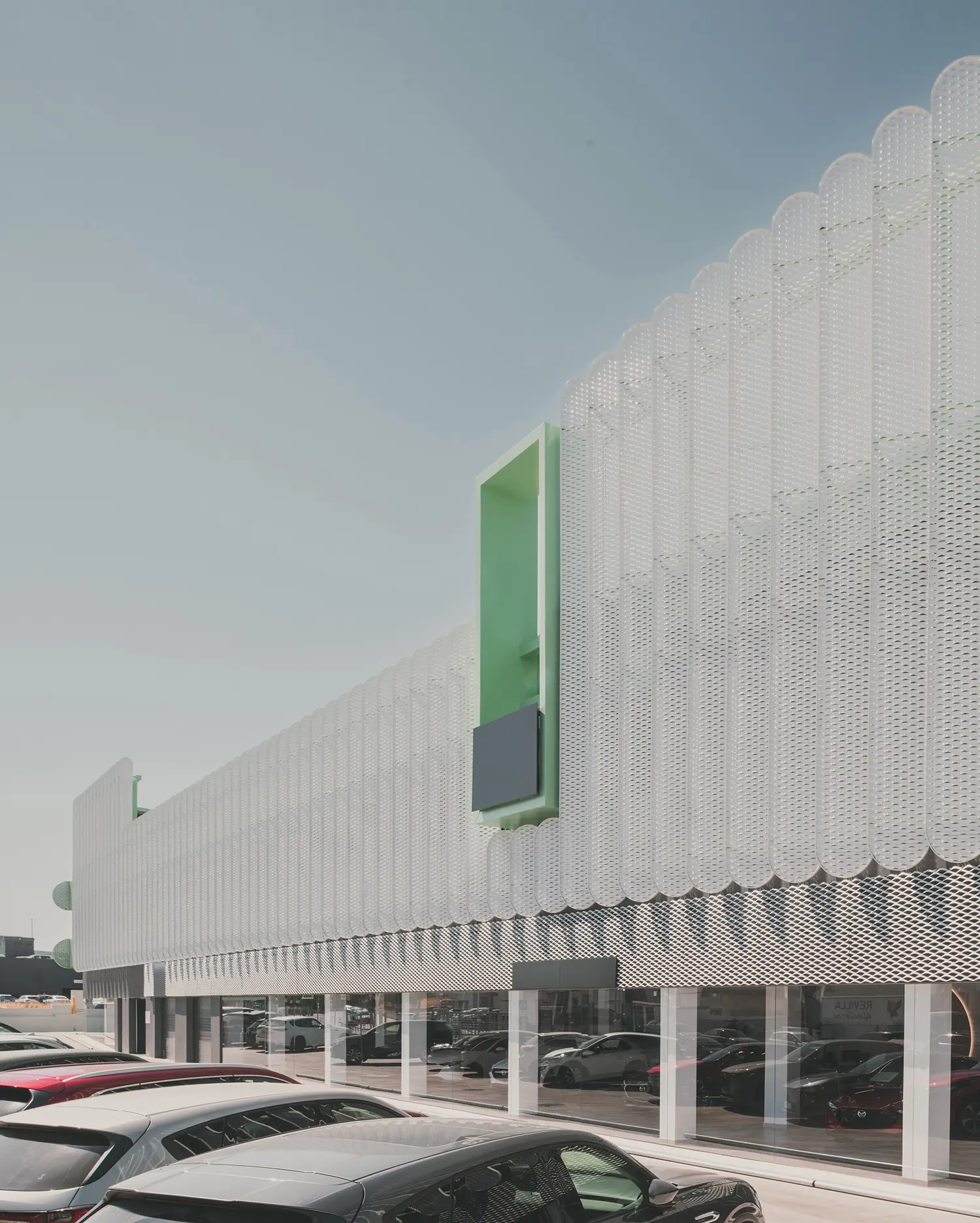 Perspective view of the white and green perforated metal skin of the Leganés Auto Center.