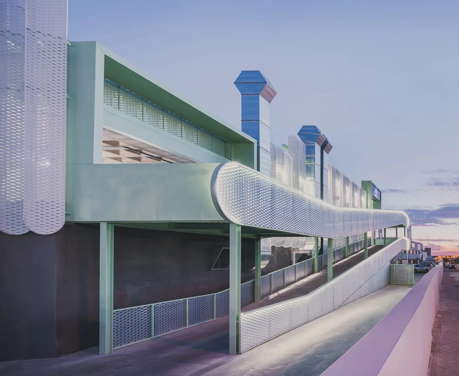 Night view of Leganés Auto Center showing the illuminated white perforated skin and green accents.